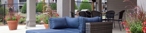 Covered outdoor lounge area at 1287 Shoals Apartments, featuring cushioned wicker seating, ceiling fan, mounted TV, and a view of the pool and landscaped courtyard in Athens, GA.