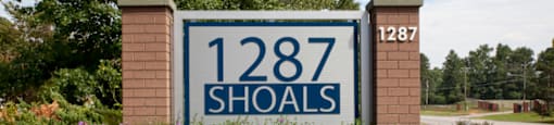 A sign for 1287 Shoals in Athens, GA is surrounded by flowers.