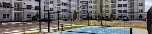 A tennis court is surrounded by apartment buildings.