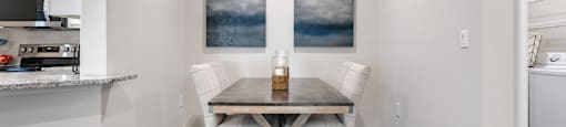 A dining room with a table and chairs and a painting on the wall.