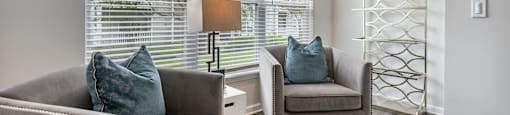 A living room with a grey couch and a chair with a blue pillow.