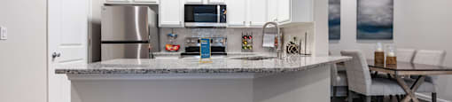 A kitchen with a stainless steel refrigerator, microwave, and white cabinets.