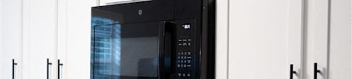 A black microwave is mounted above a black stove in a kitchen.
