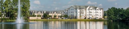 a fountain in the middle of a lake with apartment buildings in the background