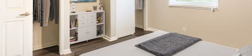 A bedroom with a bed, a ceiling fan, and a closet with clothes hanging.