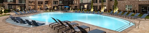 A swimming pool surrounded by lounge chairs in front of apartment buildings.