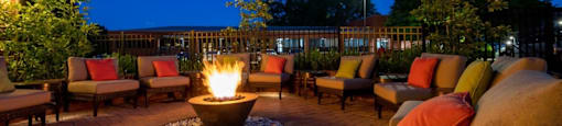 A fire pit in the middle of a patio surrounded by chairs and cushions.