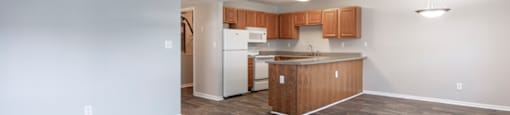 an empty living room and kitchen with wood flooring and white walls