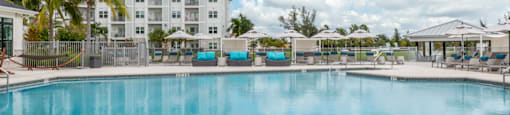 A large swimming pool surrounded by a white tiled floor and a white building in the background.