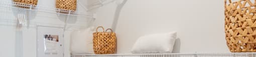 A white shelf with baskets and a white pillow.
