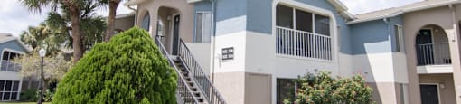 The building exterior of Park Village- two stories showing staircase, landscaping, and balcony