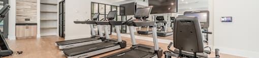 a gym with treadmills and televisions on the wall