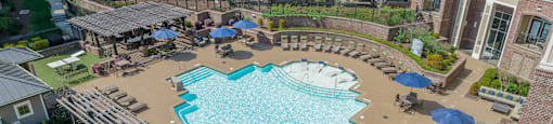a large swimming pool with lounge chairs and umbrellas in front of an apartment building