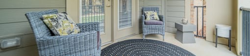 a covered porch with two chairs and a rug