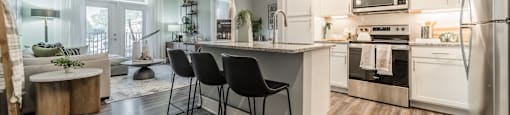 an open kitchen and living room with white cabinets and stainless steel appliances