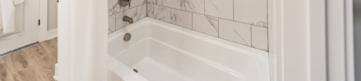 A white bathroom with a marble tile wall and a white tub.
