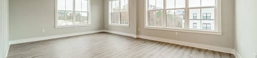 A spacious room with wooden flooring and large windows.
