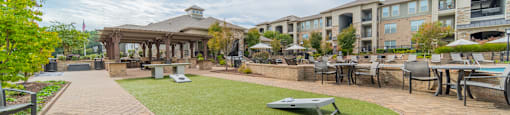 a courtyard with tables and chairs and a grassy area with buildings in the background