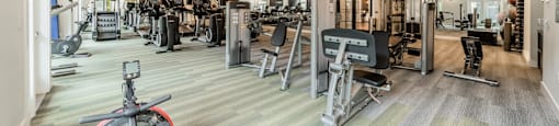 a gym with cardio machines and weights on the floor and a ceiling fan