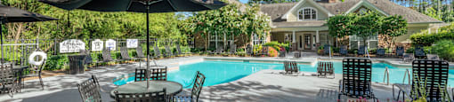 A pool area with chairs and umbrellas in front of a house.