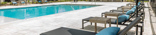 a swimming pool with chaise lounge chairs and umbrellas in front of a building