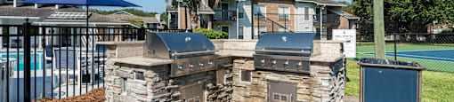 A stone fireplace with a grill on top is in the foreground of a residential area.
