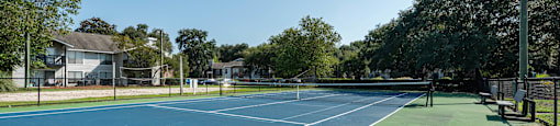 A tennis court with a blue and green surface surrounded by trees and buildings.