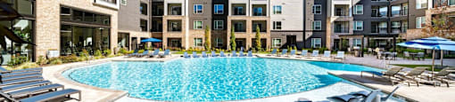 A swimming pool surrounded by lounge chairs in front of apartment buildings at Liam at Hays Farm in Huntsville, Alabama