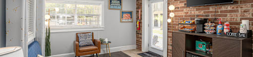 A living room with a blue couch, a brown chair, and a television mounted on the brick wall.