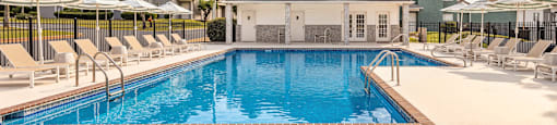 A swimming pool surrounded by lounge chairs and umbrellas with a house in the background.