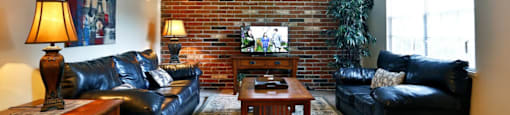 a living room with leather furniture and a brick wall