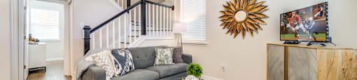 A living room with a grey couch, a glass coffee table, a wooden cabinet, and a wall art.