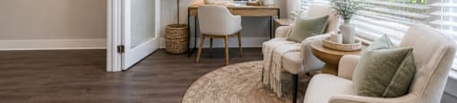 A cozy living room with a white chair, a brown table, and a small tree.