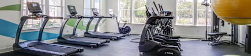 a gym with cardio equipment and a ceiling fan