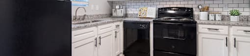 A black refrigerator stands next to a kitchen counter with white cabinets and a black oven.