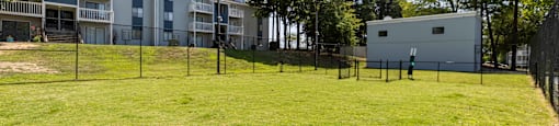 A dog park with a building and trees in the background at Enclave at 38 Twenty Two Apartments in Greensboro, NC