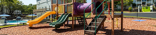 A playground with a yellow slide, a purple slide, and a red and yellow playhouse at Enclave at 38 Twenty Two Apartments in Greensboro, NC