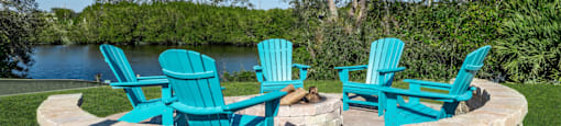 a fire pit with three adirondack chairs and a lake in the background