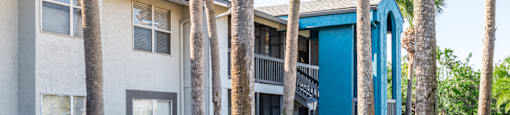 a building with a blue and white exterior and a sidewalk and palm trees in front of it