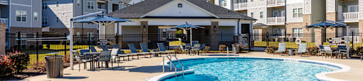 A swimming pool surrounded by a concrete patio and lounge chairs.