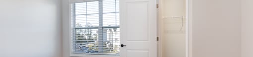A room with a white door and a window with blinds.