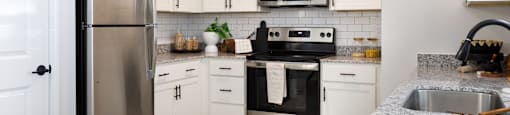 A kitchen with a refrigerator, microwave, oven, and sink.
