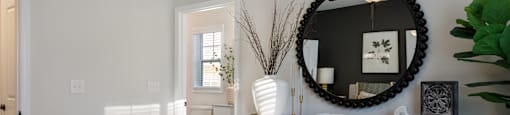 A bedroom with a bed, dresser, mirror, and plants.