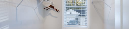 A white closet with a window showing a house and trees outside.