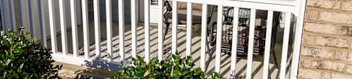 A white railing with a fan and plants on a porch.