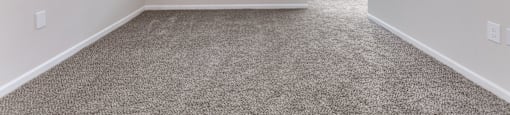 A room with a carpeted floor and a window with blinds.