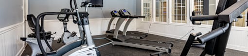 A home gym with a treadmill, elliptical trainer, and a fan.
