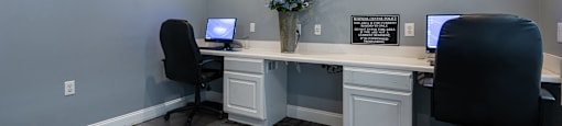 A room with two computers and a vase of flowers on the desk.
