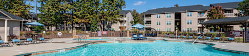 A large swimming pool surrounded by trees and apartment buildings.