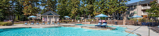 A large swimming pool surrounded by trees and a building in the background.